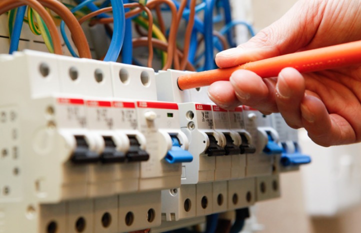 Elektryk w trakcie sprawdzania bezpieczników w skrzynce rozdzielczej przy użyciu próbnika napięcia z pomarańczową rączką.