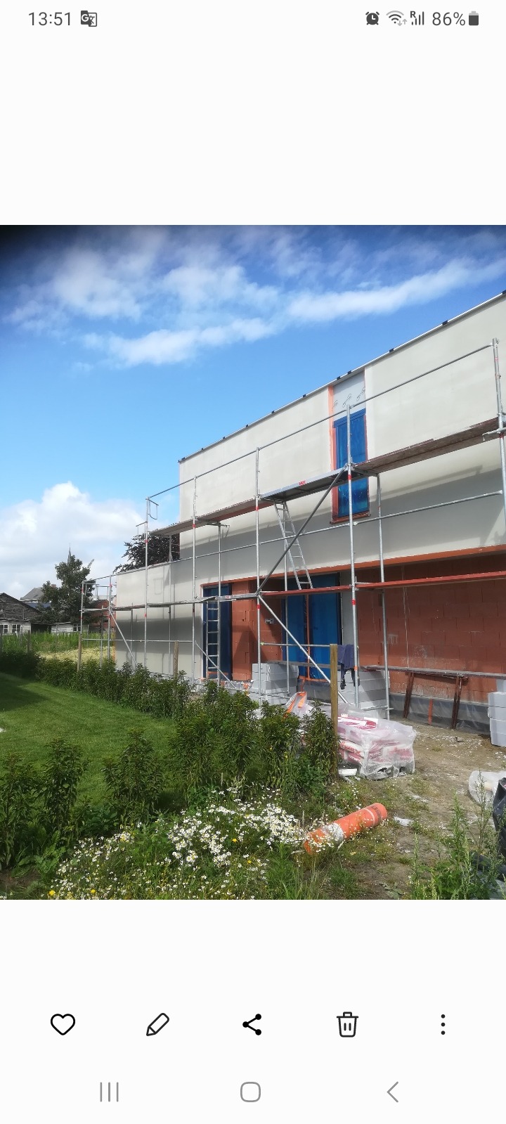 Budynek w trakcie prac elewacyjnych, widoczne rusztowania, częściowo otynkowana fasada i materiały budowlane w ogrodzie