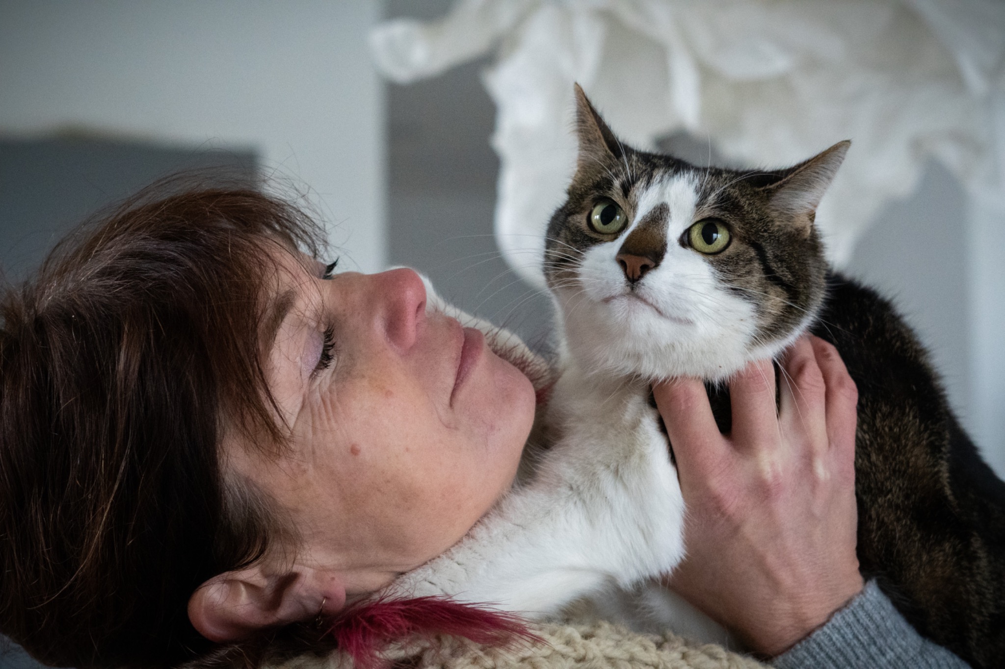 Kobieta z bliska, leżąca na boku, trzymająca pod szyją brązowo-białego kota z zielonymi oczami, patrzącego w górę.