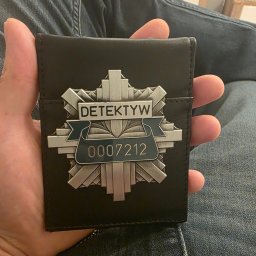 Agencja Detektywistyczna Biuro bezpieczeństwa SPECTRUM & Detektyw NOWICKI - Czarny portfel z odznaką z napisem 'Detektyw' i numerem 0007212, trzymany w dłoni na tle dżinsów. Prezentacja licencji detektywistycznej.