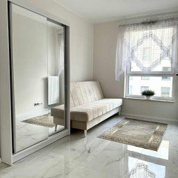 R-Style usługi remontowo-wykończeniowe Rafał Wyrzykowski - Jasne wnętrze pokoju z marmurową podłogą, beżową sofą i szafą z lustrem. Okno z koronkową firanką i dywan dodają przytulności. Nowoczesne oświetlenie sufitowe.