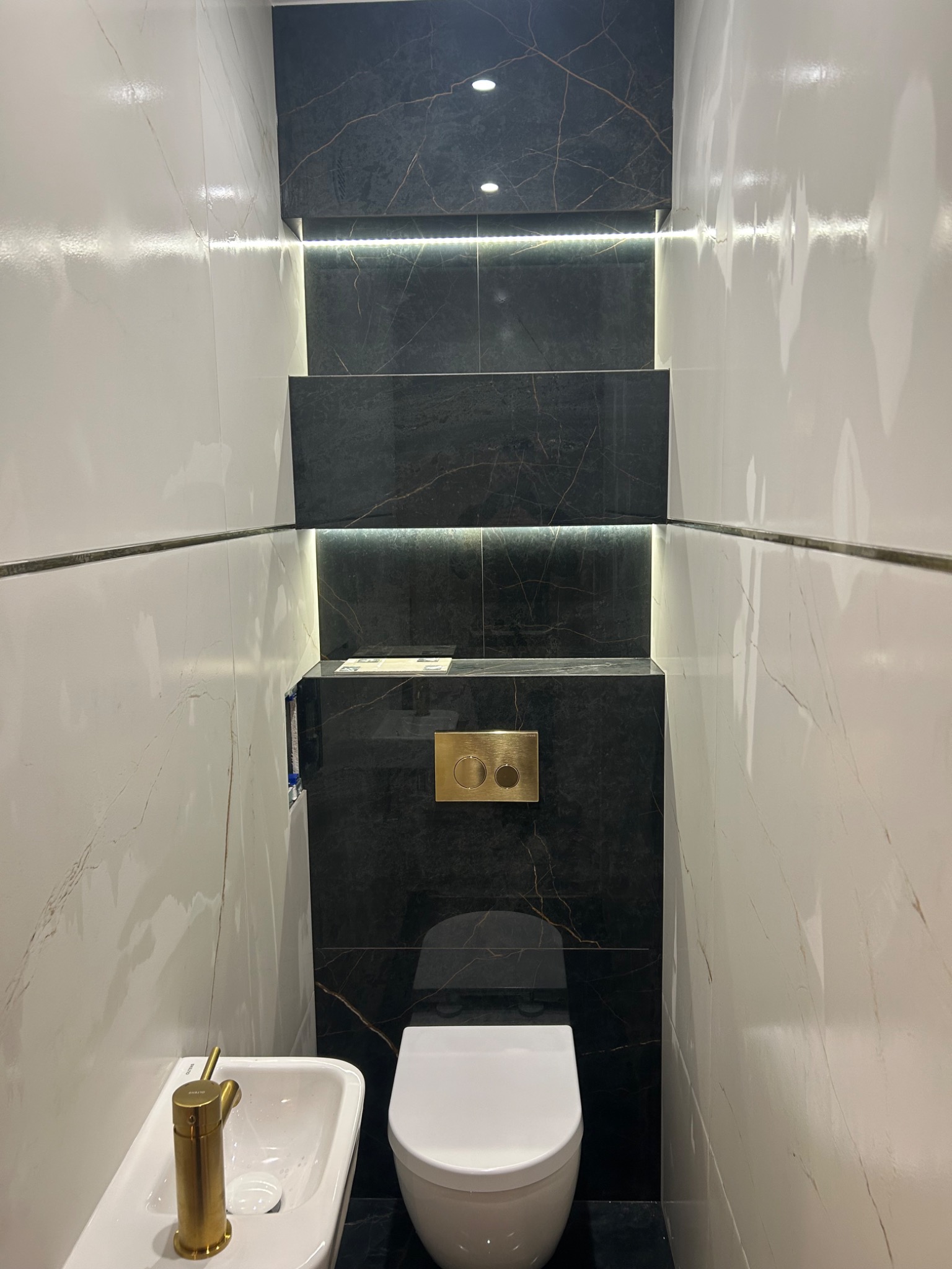 Elegancka łazienka w Leszczydół-Nowiny z czarno-białymi płytkami imitującymi marmur, podświetleniem LED i złotą armaturą. Nowoczesny design.