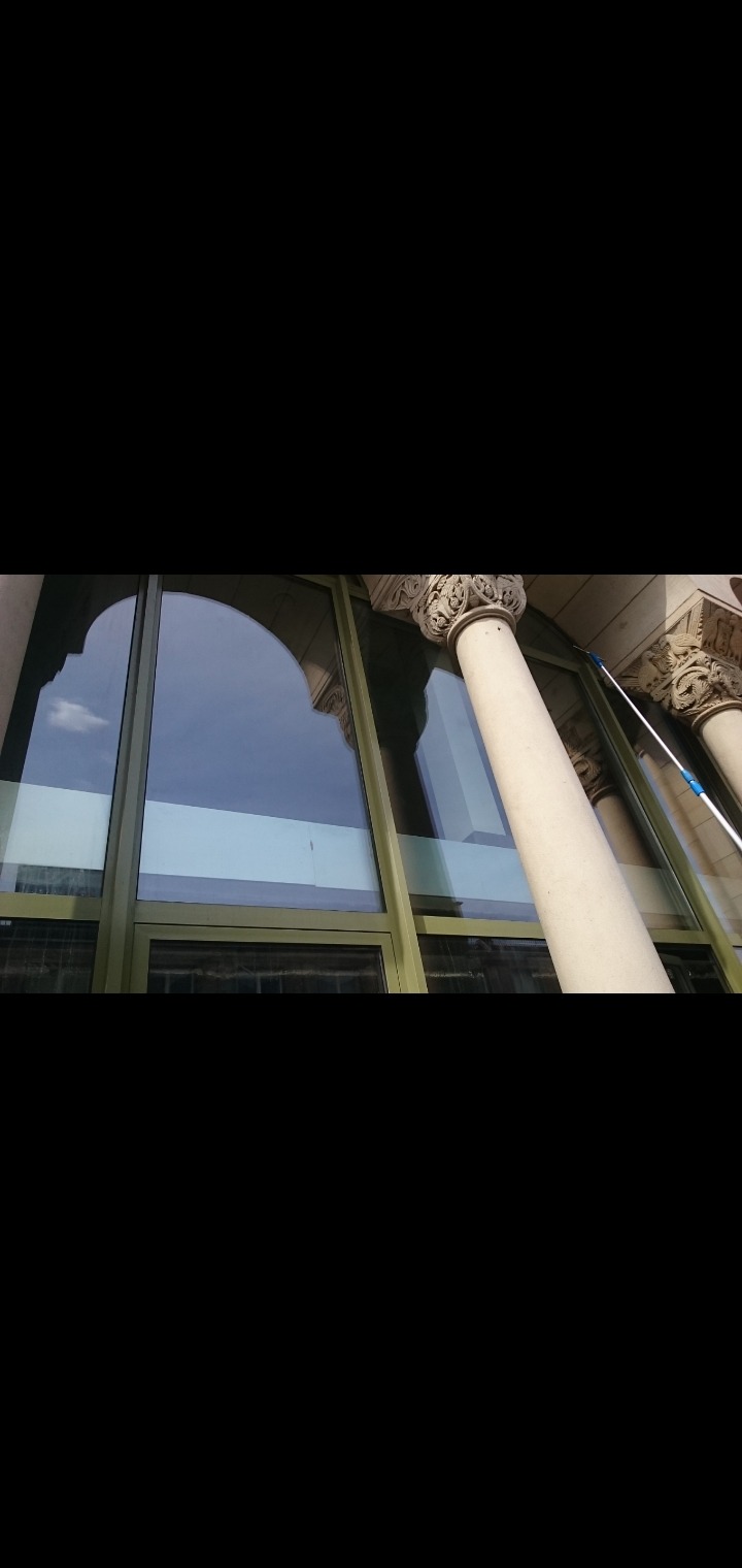 Czyszczenie dużych okien w budynku z kolumnami, widoczny fragment kija do mycia okien.