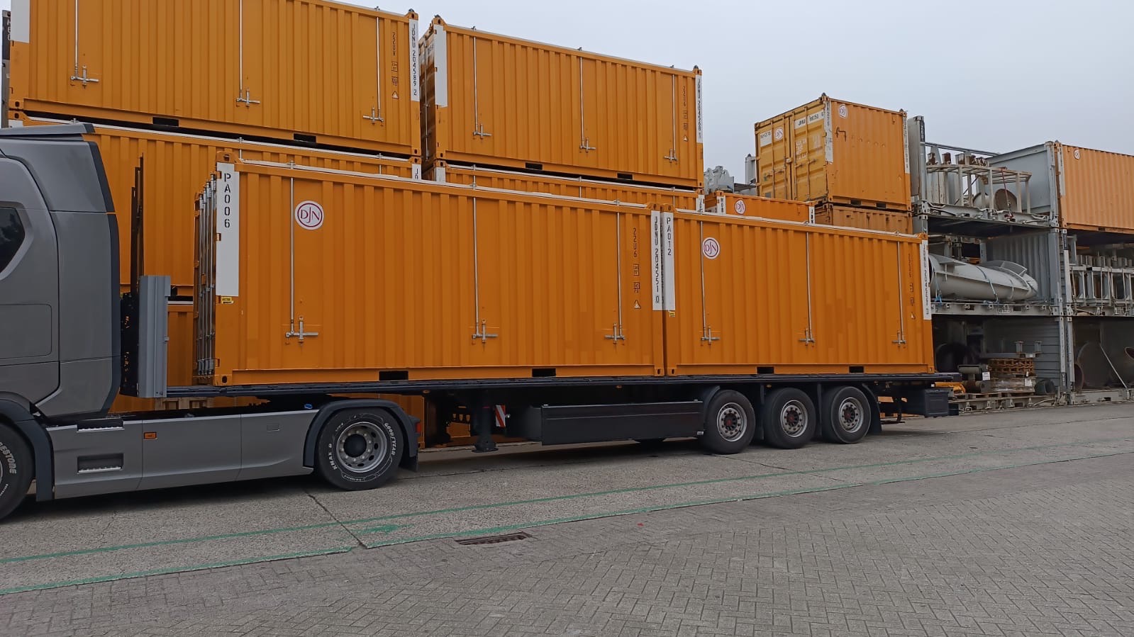 Ciężarówka z naczepą przewożąca pomarańczowe kontenery transportowe, widoczne oznaczenia PA006 i DJN na kontenerach.