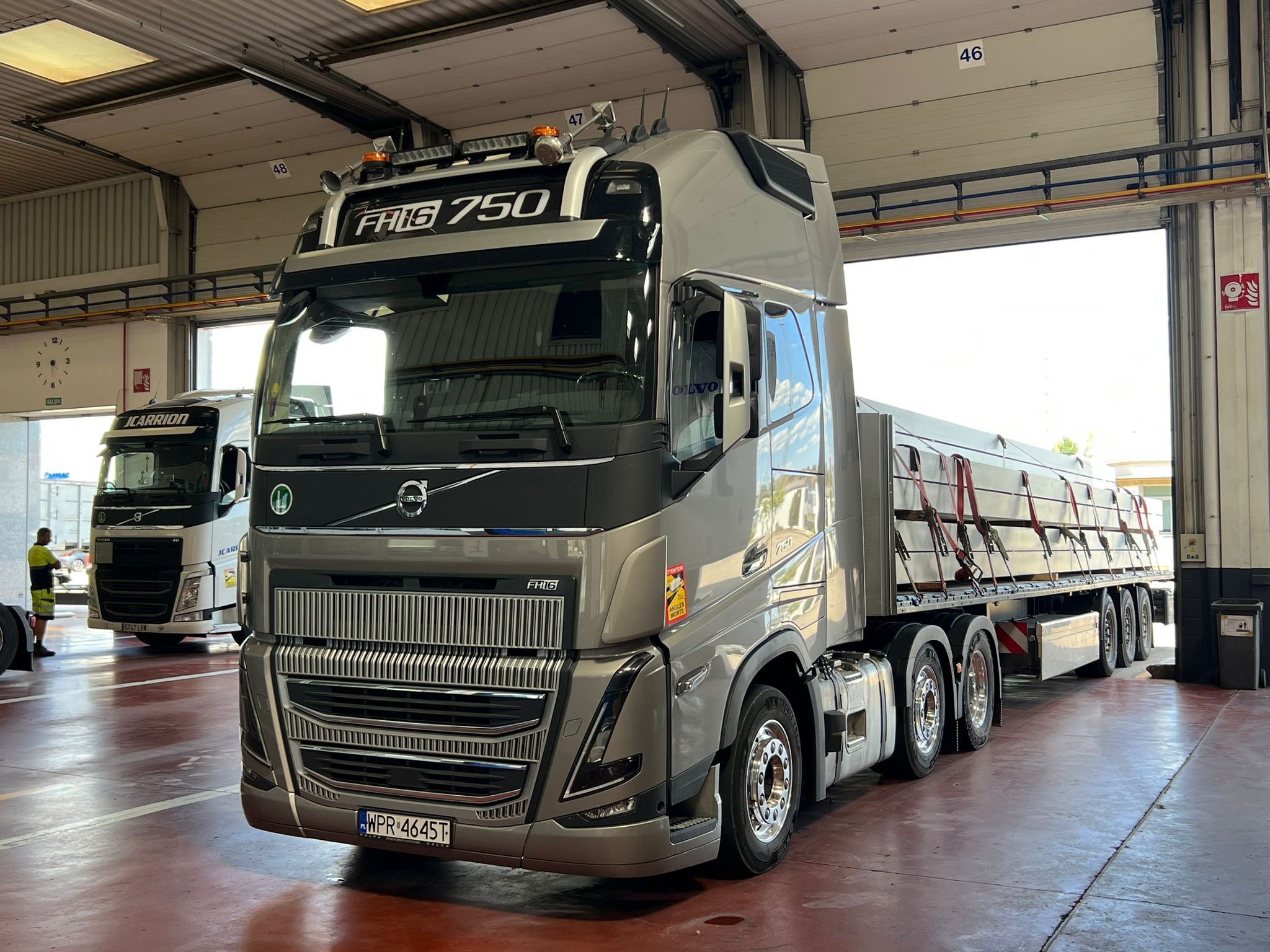 Szary ciągnik siodłowy Volvo FH16 750 z naczepą przewożącą ładunek, zaparkowany w hali w Elblągu, widoczne tablice rejestracyjne z Polski.