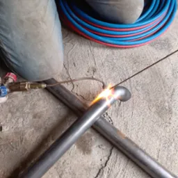 Spawanie rur w Szemudzie: zbliżenie na proces łączenia metalowych elementów, widoczny palnik i iskry, obok zwój czerwono-niebieskich węży.