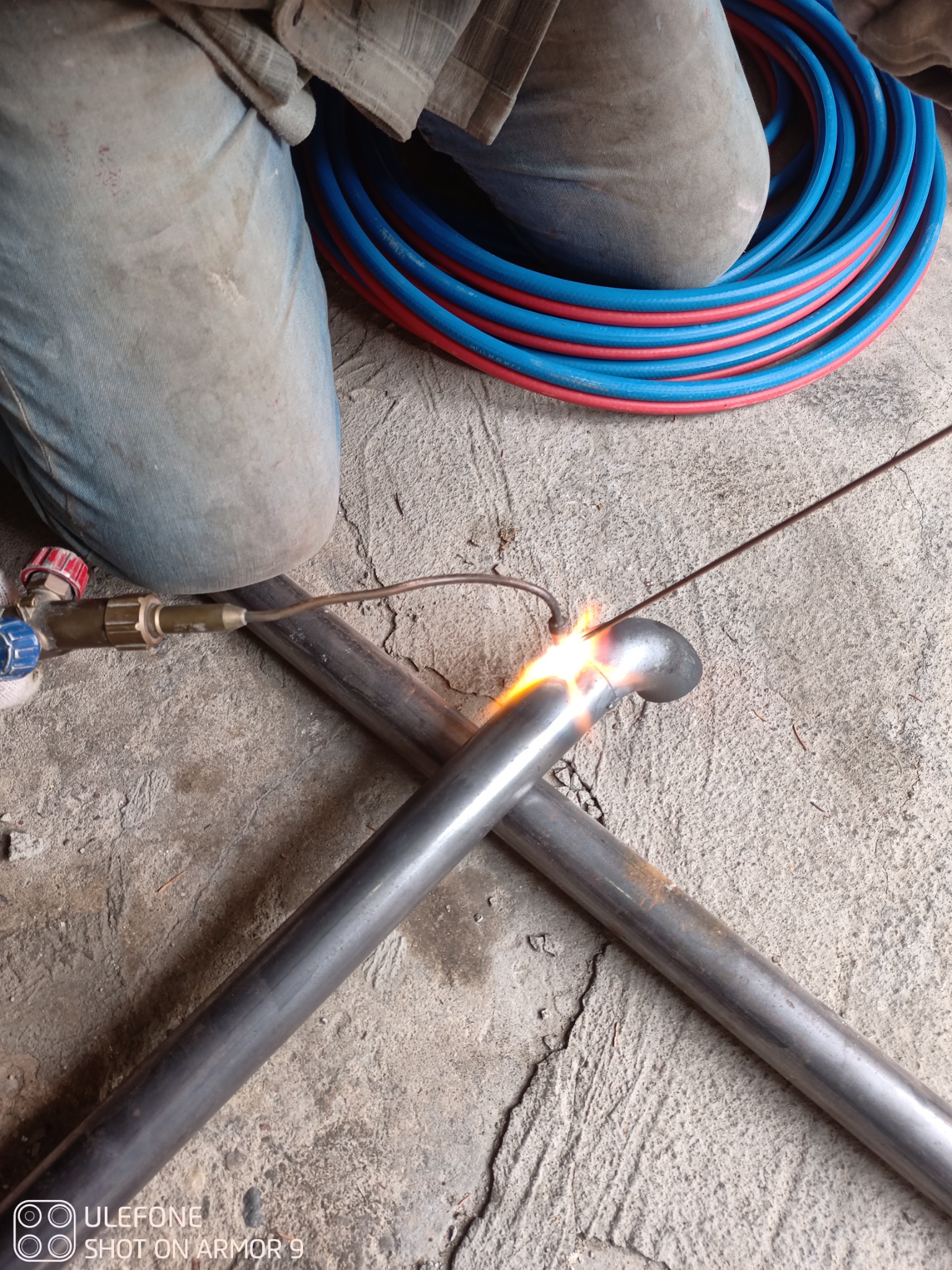 Spawanie rur w Szemudzie: zbliżenie na proces łączenia metalowych elementów, widoczny palnik i iskry, obok zwój czerwono-niebieskich węży.