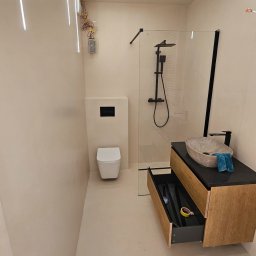 Nowoczesna łazienka z liniowym oświetleniem LED, kabiną prysznicową typu walk-in, umywalką nablatową i szafką z otwartą szufladą. Minimalistyczny design, beżowe ściany.