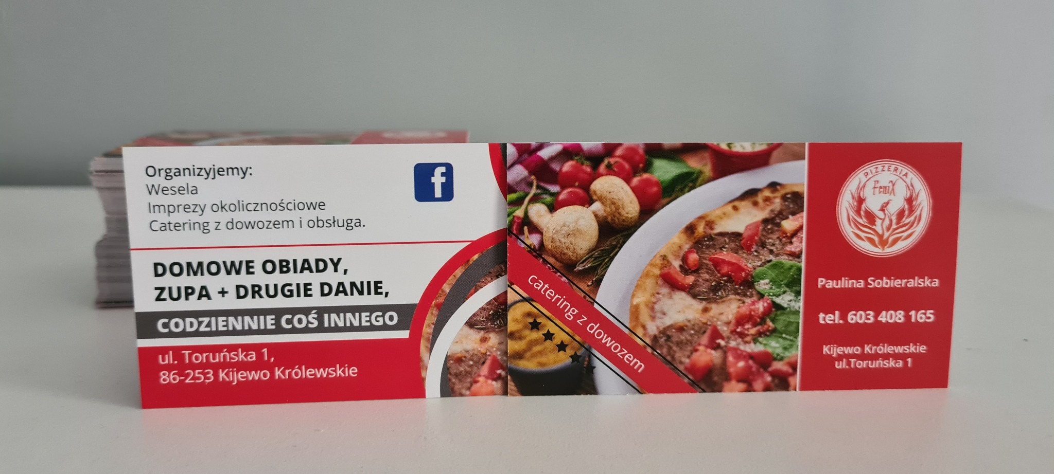 Stos wizytówek pizzerii z ofertą cateringową, domowych obiadów i imprez okolicznościowych, z elementami graficznymi pizzy i logo firmy.