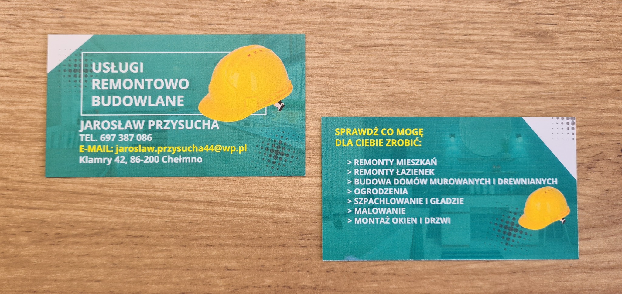 Dwie wizytówki firmy remontowo-budowlanej z żółtym kaskiem, na drewnianym tle. Jedna wizytówka prezentuje dane kontaktowe, druga listę oferowanych usług.