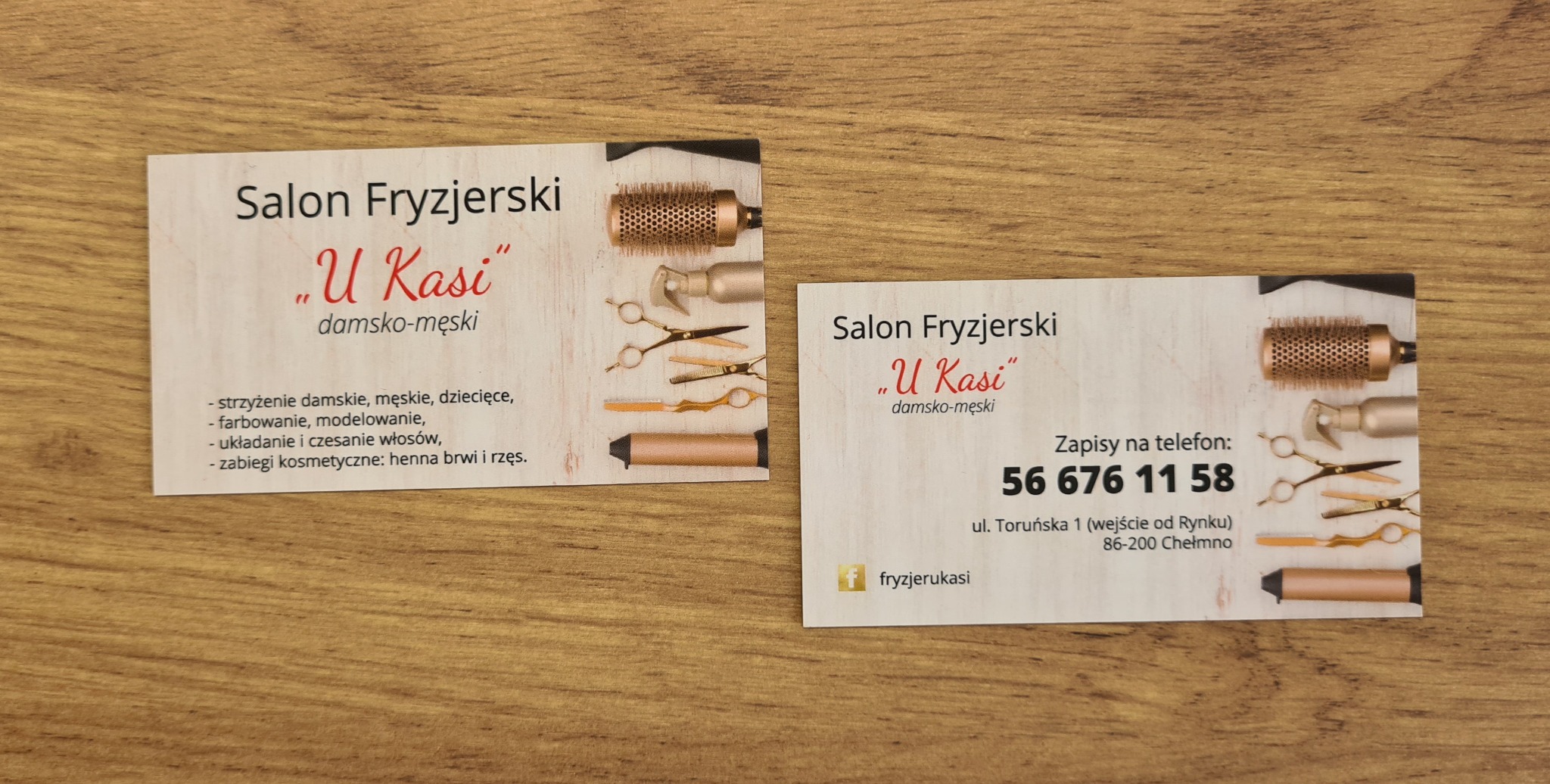 Dwie wizytówki salonu fryzjerskiego 'U Kasi' leżące na drewnianym blacie. Wizytówki zawierają informacje o salonie, numer telefonu i adres. Na jednej z wizytówek widoczne grafiki przedstawiające...