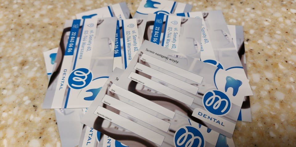 Stos wizytówek gabinetu stomatologicznego z logo w kolorze niebieskim i miejscem na wpisanie terminu następnej wizyty.