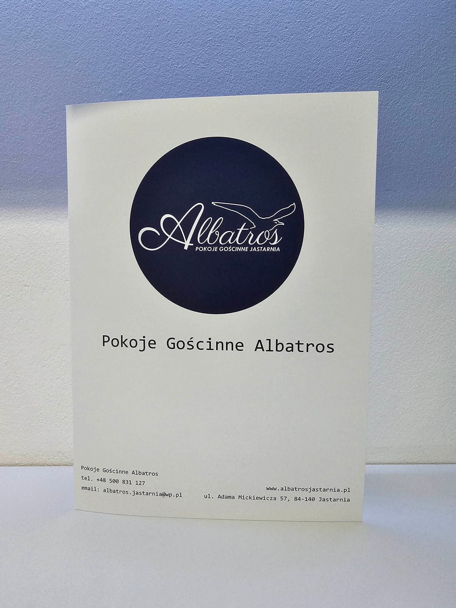Biała ulotka reklamowa z granatowym logo Albatros i informacjami kontaktowymi dla pokoi gościnnych w Jastarni, ustawiona pionowo na białym tle.