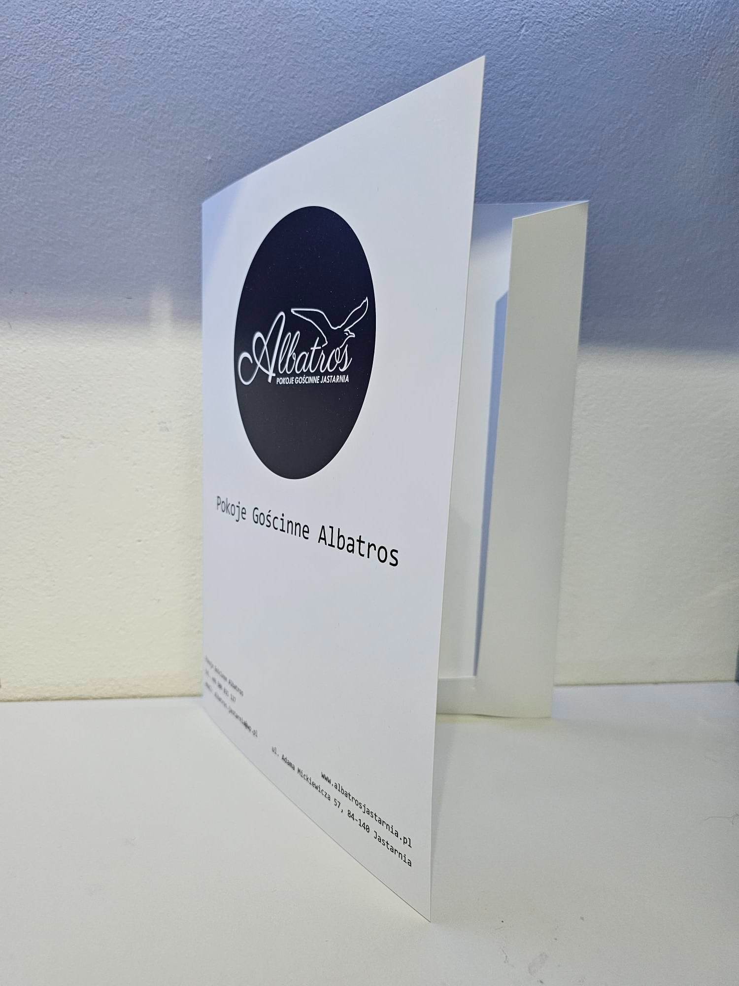 Biała, otwarta ulotka reklamowa z logo i danymi kontaktowymi pensjonatu Albatros w Jastarni, umieszczona na jasnym tle.