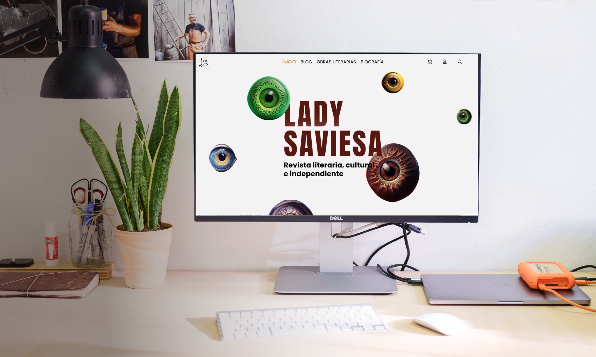 Monitor Dell wyświetlający stronę internetową 'Lady Saviesa', literackiego magazynu online, na biurku z rośliną, klawiaturą i dyskiem zewnętrznym.