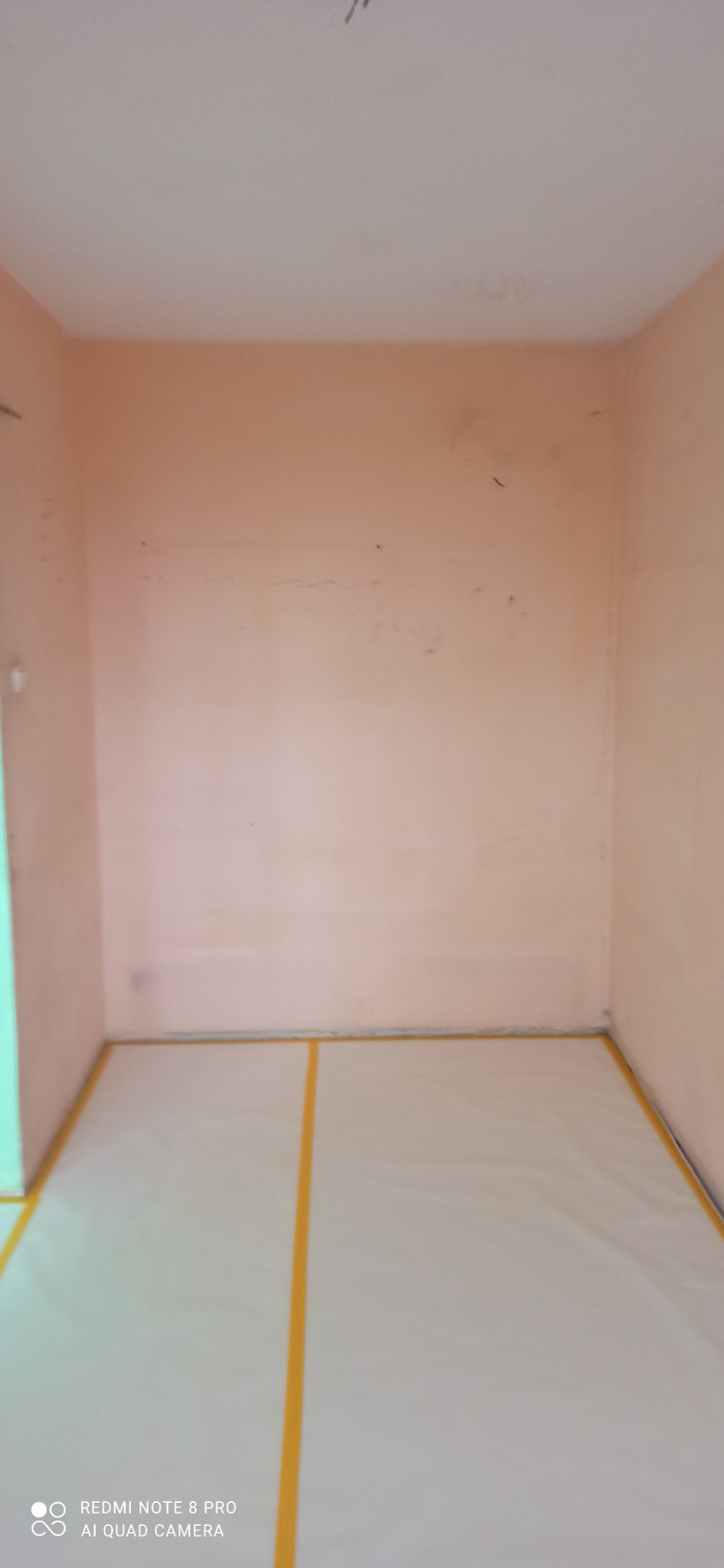 Pokój przygotowany do malowania: podłoga zabezpieczona folią i taśmą malarską, ściany w odcieniach różu, widoczne ślady po wcześniejszych pracach.