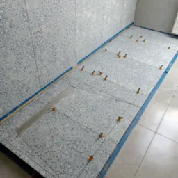 Podczas układania płytek z geometrycznym wzorem w łazience, widoczny odpływ liniowy i system poziomowania płytek z pomarańczowymi klinami.