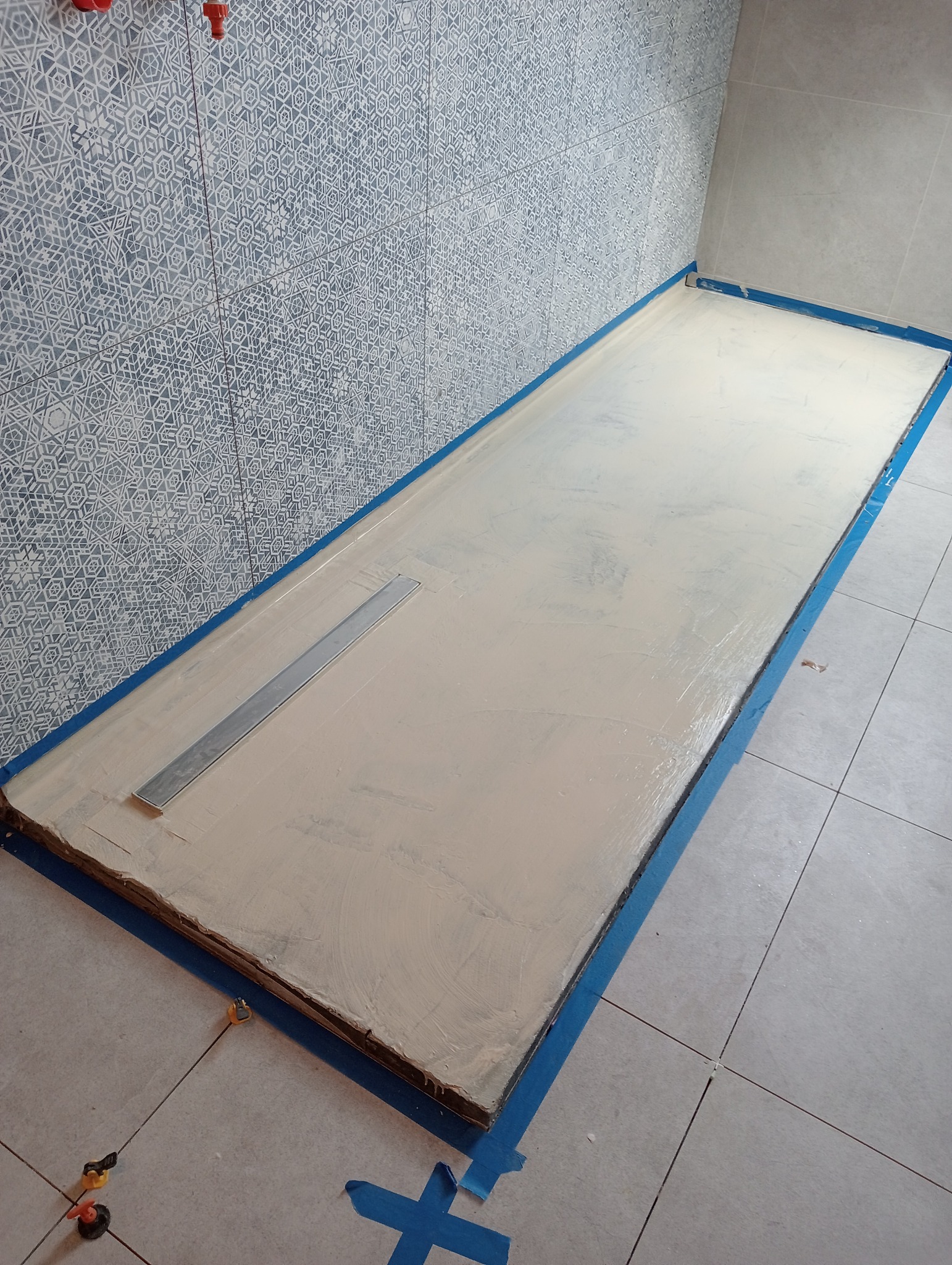 Przygotowany brodzik z odpływem liniowym, zabezpieczony niebieską taśmą malarską, w trakcie wylewania posadzki w łazience z dekoracyjnymi płytkami ściennymi.