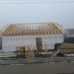 Konstrukcja drewniana dachu w trakcie budowy domu, zabezpieczona membraną Tyvek, widok w pochmurny dzień.