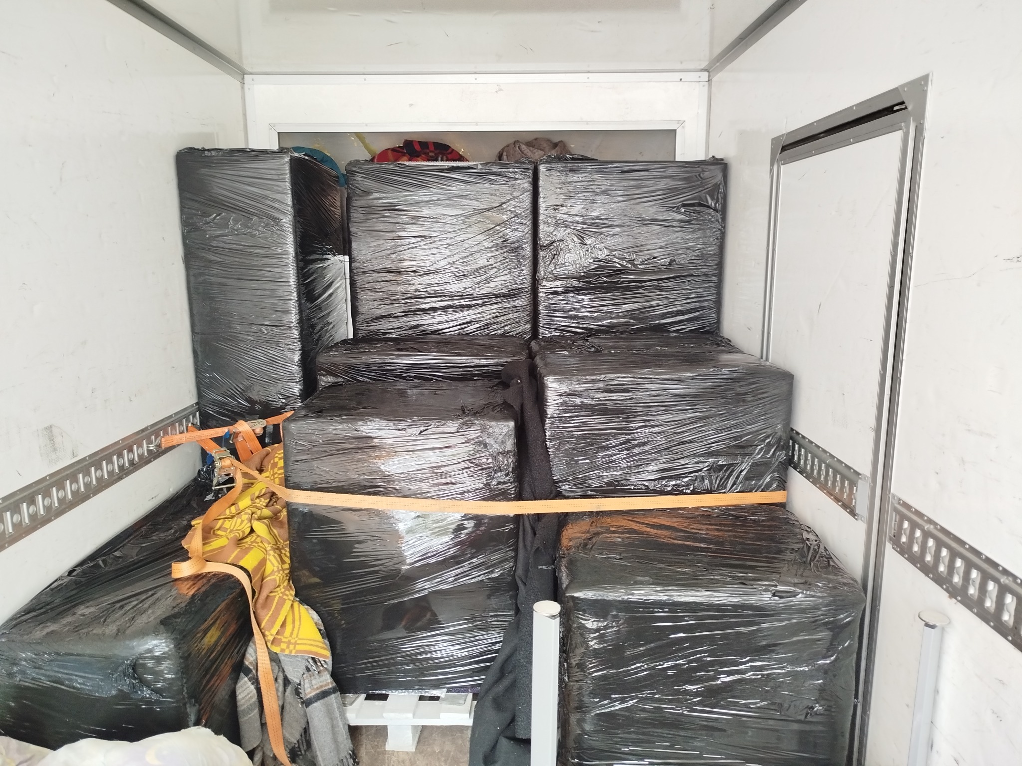 Ładunek zabezpieczony folią i pasami wewnątrz białej furgonetki transportowej, gotowy do przewozu. Widoczne mocowania na ścianach pojazdu.