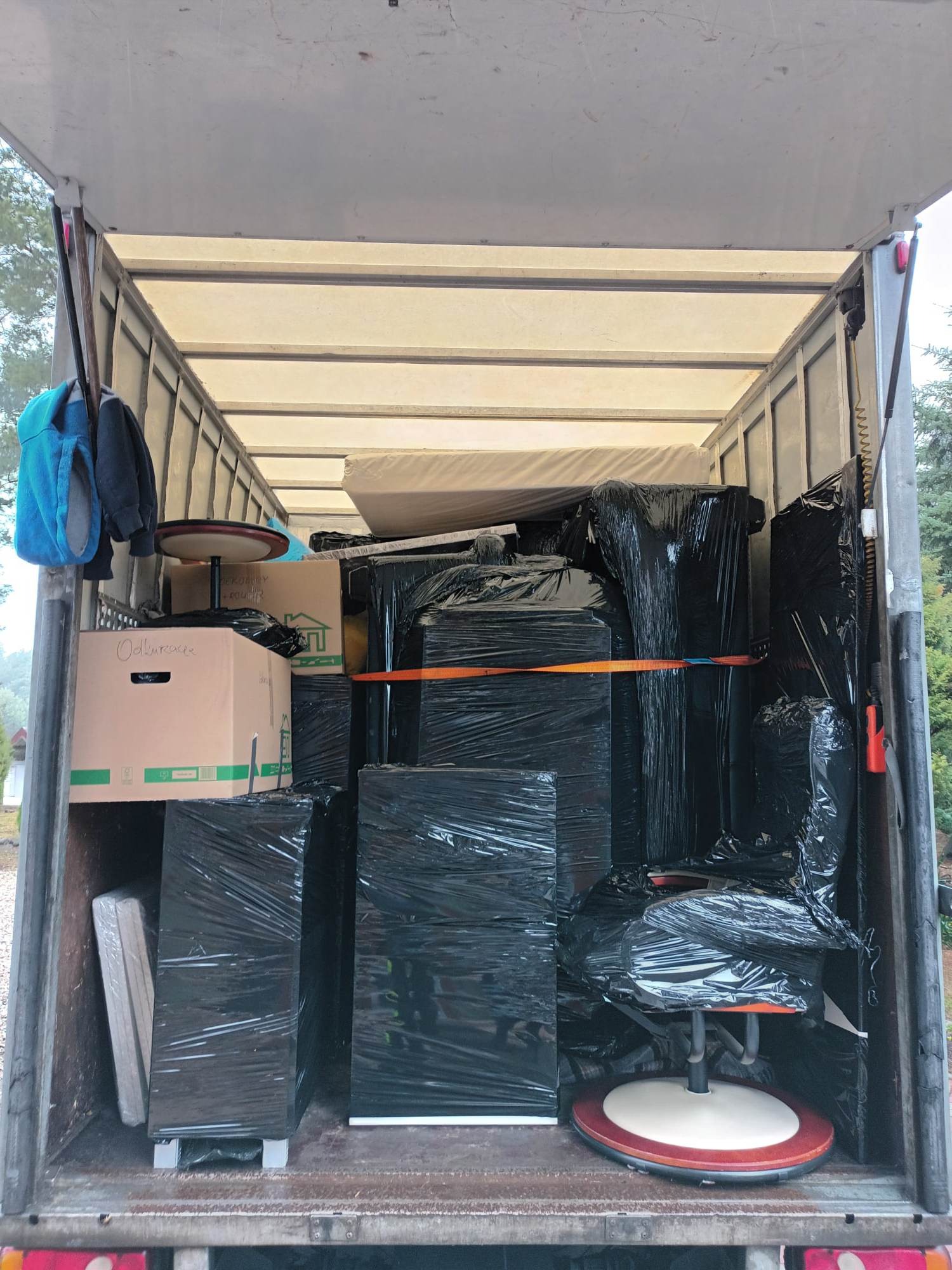 Wnętrze furgonetki wypełnionej meblami i kartonami zabezpieczonymi folią stretch oraz pasami transportowymi, gotowymi do transportu podczas przeprowadzki.