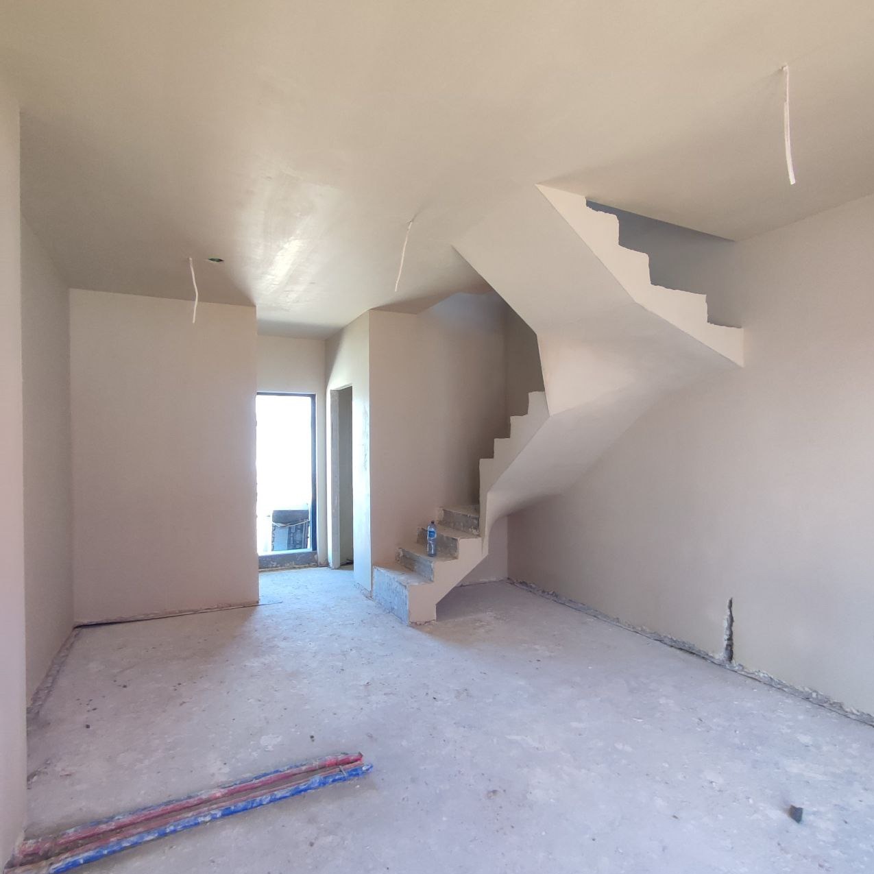 Wnętrze domu po nałożeniu gładzi gipsowej, widoczne schody ze śladami po pracach, wystające kable i rury na podłodze.