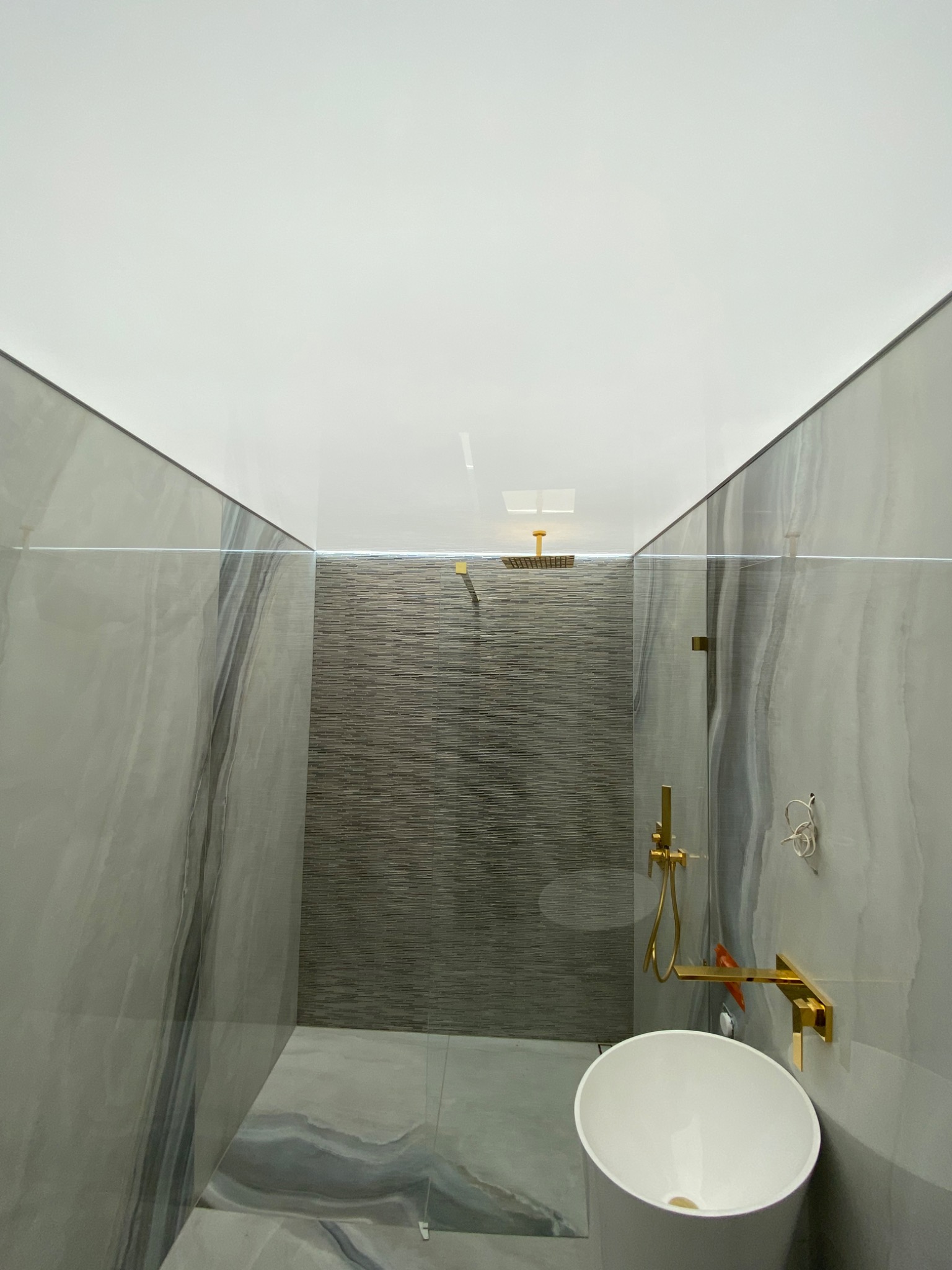 Nowoczesna łazienka z kabiną prysznicową typu walk-in, wykończona płytkami imitującymi marmur i szarą mozaiką, z armaturą w kolorze złotym i umywalką nablatową.