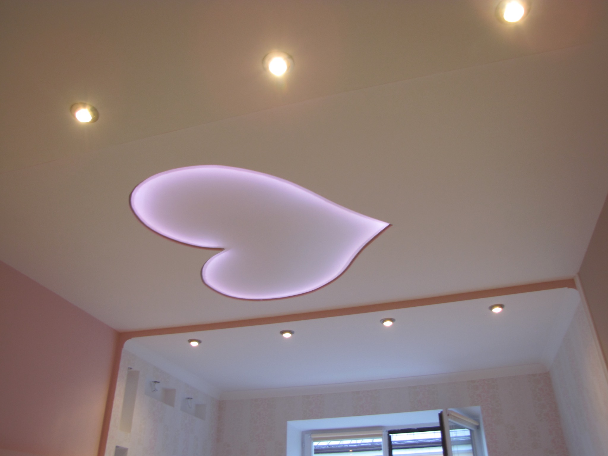 Biały sufit z wbudowanym oświetleniem punktowym i podświetlanym motywem serca w kolorze fioletowym, widok z dołu.