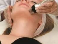 Klientka podczas zabiegu medycyny estetycznej na twarz, wykonywanego przez osobę w rękawiczkach ochronnych przy użyciu specjalistycznego urządzenia.