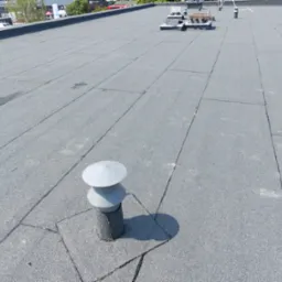 Płaski dach pokryty papą termozgrzewalną z widocznymi kominkami wentylacyjnymi i elementami wentylacji kalenicy, w tle budynki.