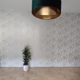 Pokój z tapetą w motywie drzew, zielonymi drzwiami i lampą z zielonym abażurem, uzupełniony rośliną doniczkową.