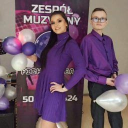 Zespół Muzyczny Fighter Team - Dwoje młodych ludzi w fioletowych strojach pozuje na tle baneru z napisem 'Zespół Muzyczny', trzymając fioletowe i białe balony.