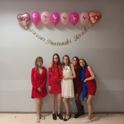 Zespół Muzyczny Fighter Team - Pięć kobiet pozuje do zdjęcia na tle ściany z balonami i napisem 'Wieczór Panieński Monki', ubrane w sukienki i boa, jedna z szarfą 'Bride to be'.