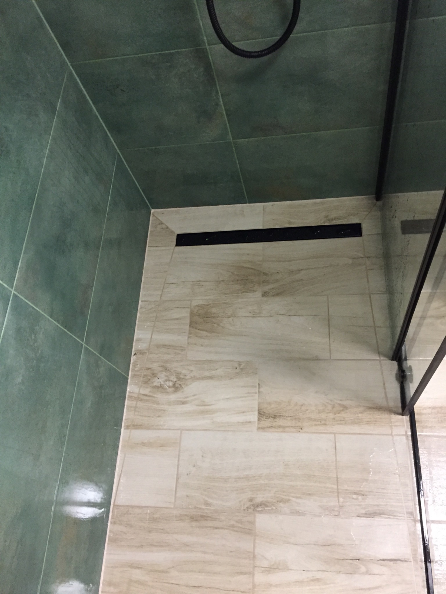 Kabina prysznicowa z odpływem liniowym, wyłożona płytkami w odcieniach zieleni i beżu, widok z góry.