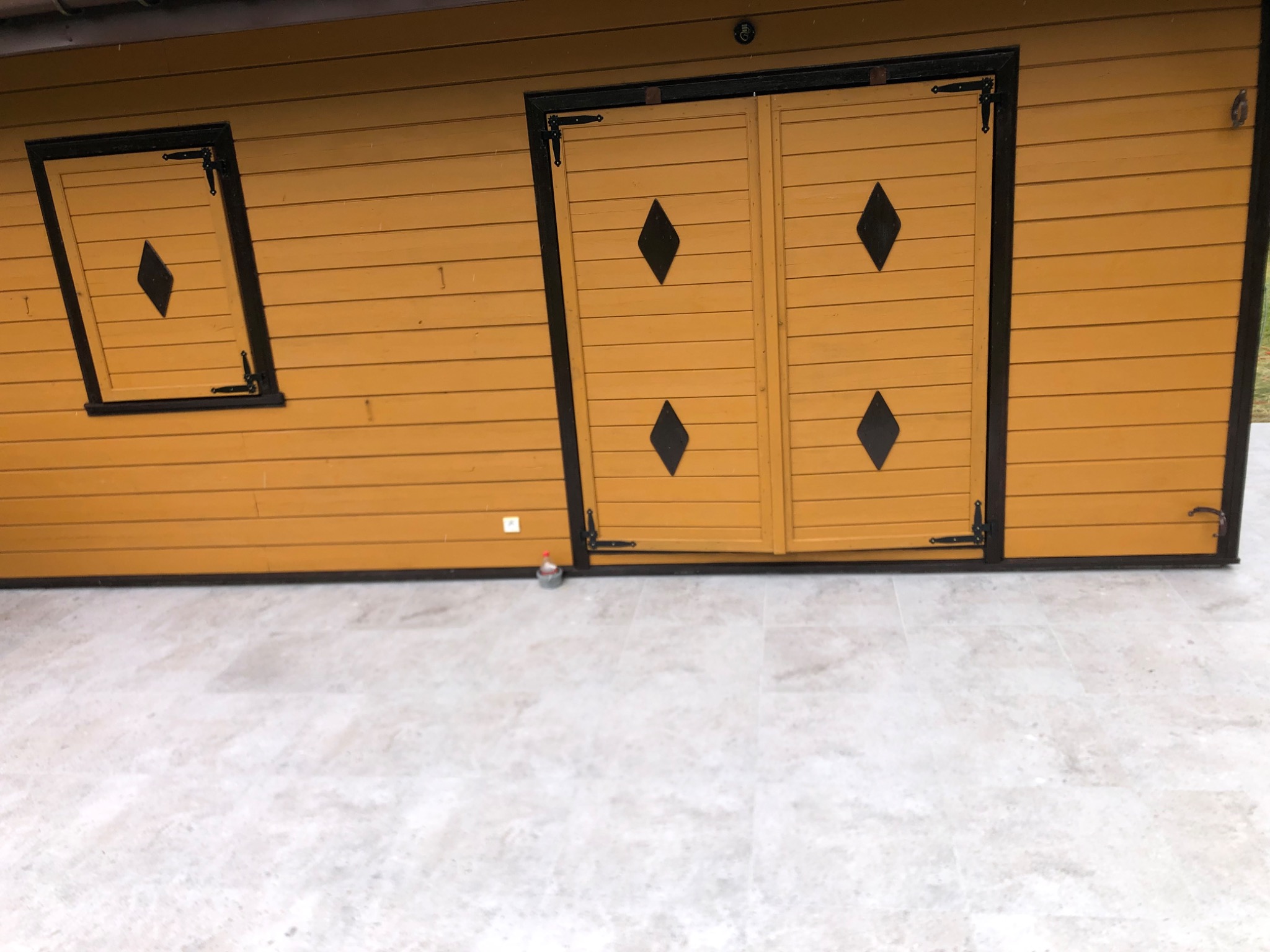 Żółta drewniana elewacja budynku z czarnymi zdobieniami okien i drzwi, wykończona jasną marmurową posadzką.