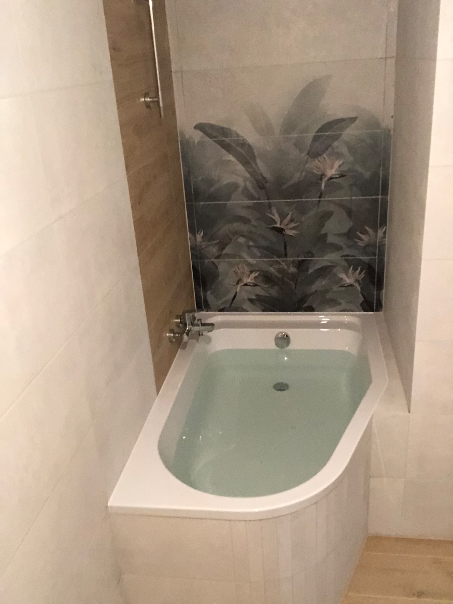 Nowoczesna łazienka w Warszawie z wanną wypełnioną wodą, wykończona płytkami z motywem roślinnym i drewnopodobnymi panelami ściennymi.