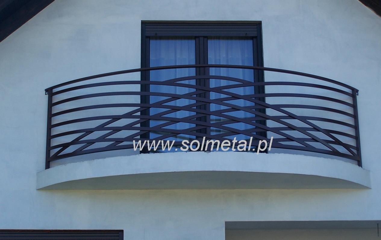 Balkon z metalową, giętą balustradą w kolorze grafitowym, umieszczony na białej elewacji budynku, z widocznym oknem za balustradą i adresem strony internetowej nałożonym na zdjęcie.