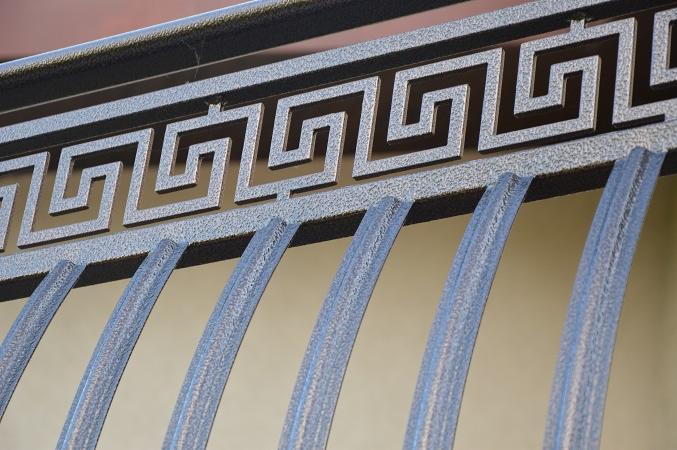 Metalowa balustrada z geometrycznym wzorem w stylu greckim, pomalowana na srebrno-szary kolor, widoczna z bliska.