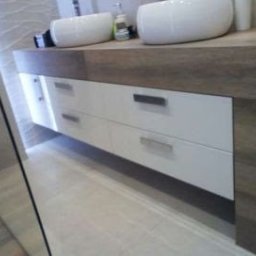 Meble Lili - Łazienka z dwiema umywalkami nablatowymi, zamontowanymi na blacie z drewnopodobnym wykończeniem. Białe, lakierowane fronty szuflad z minimalistycznymi, metalowymi uchwytami. Podświetlenie LED...