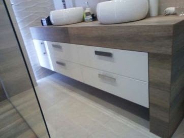 Łazienka z dwiema umywalkami nablatowymi, zamontowanymi na blacie z drewnopodobnym wykończeniem. Białe, lakierowane fronty szuflad z minimalistycznymi, metalowymi uchwytami. Podświetlenie LED...