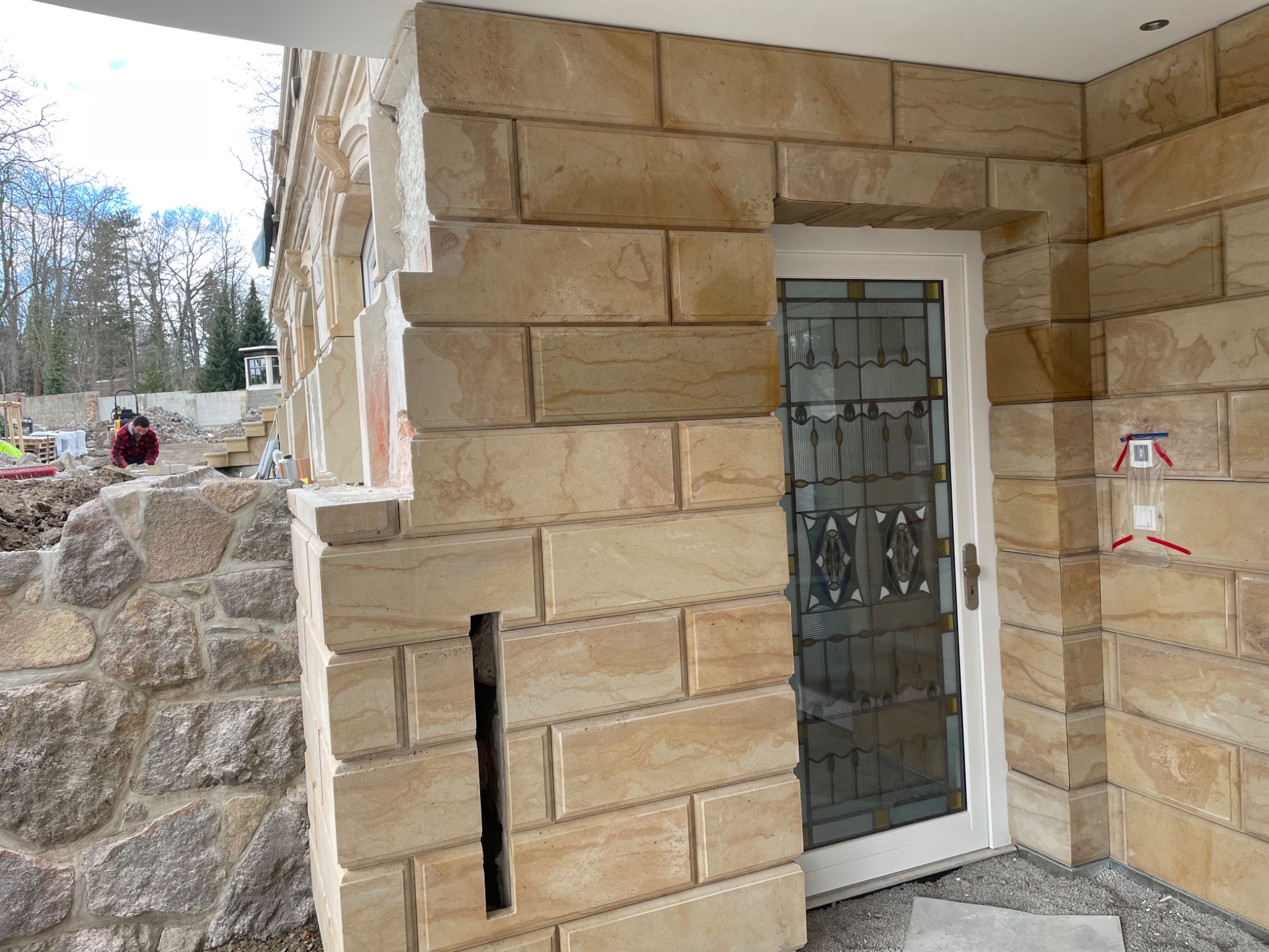 Murowana elewacja z piaskowca w Mirsku, z widocznym fragmentem drzwi wejściowych z ozdobnym szkłem oraz pracującym robotnikiem w tle.