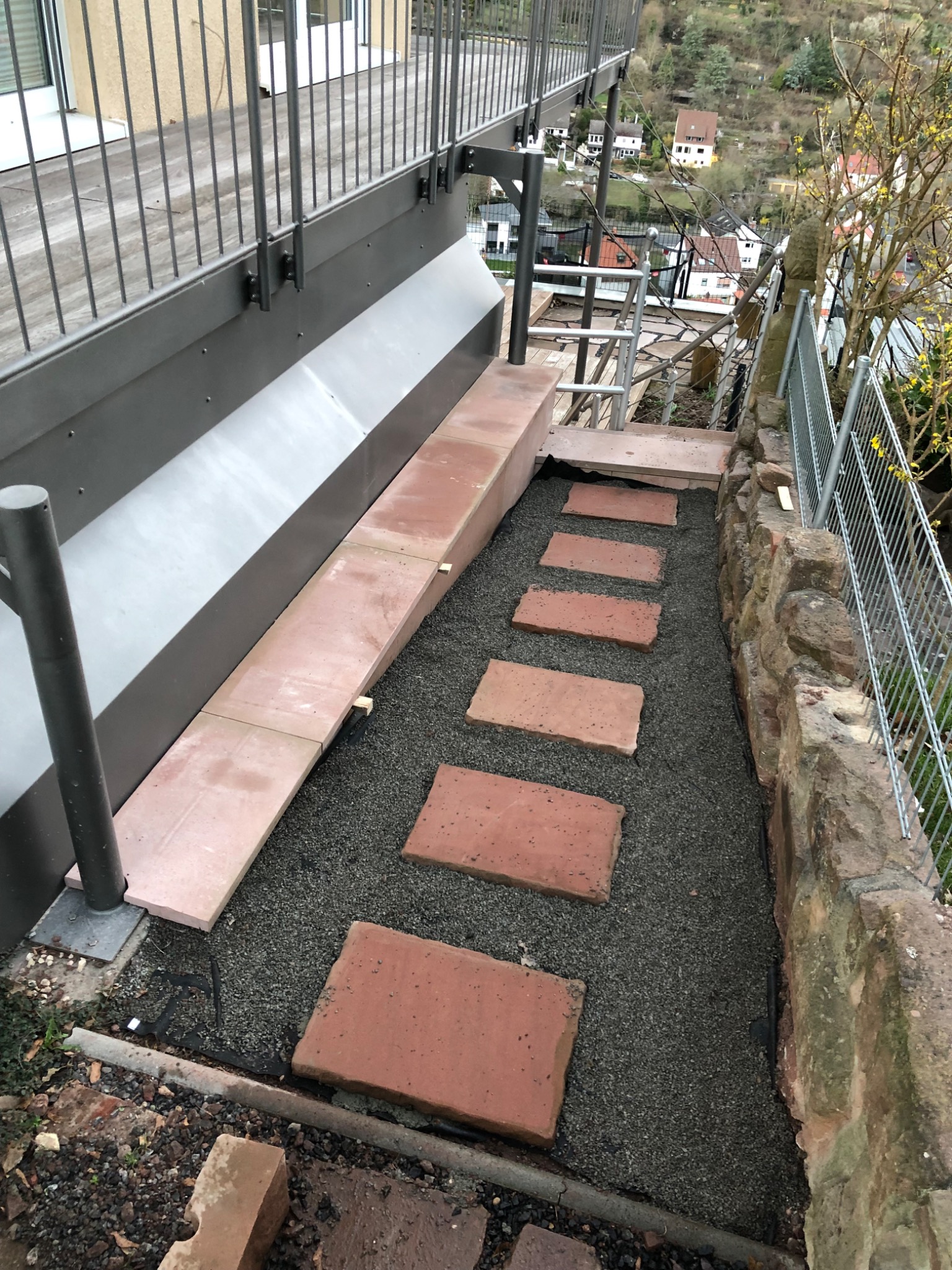 Schody zewnętrzne z czerwonych płyt kamiennych ułożonych na żwirze, prowadzące z balkonu w dół zbocza, widok z góry.