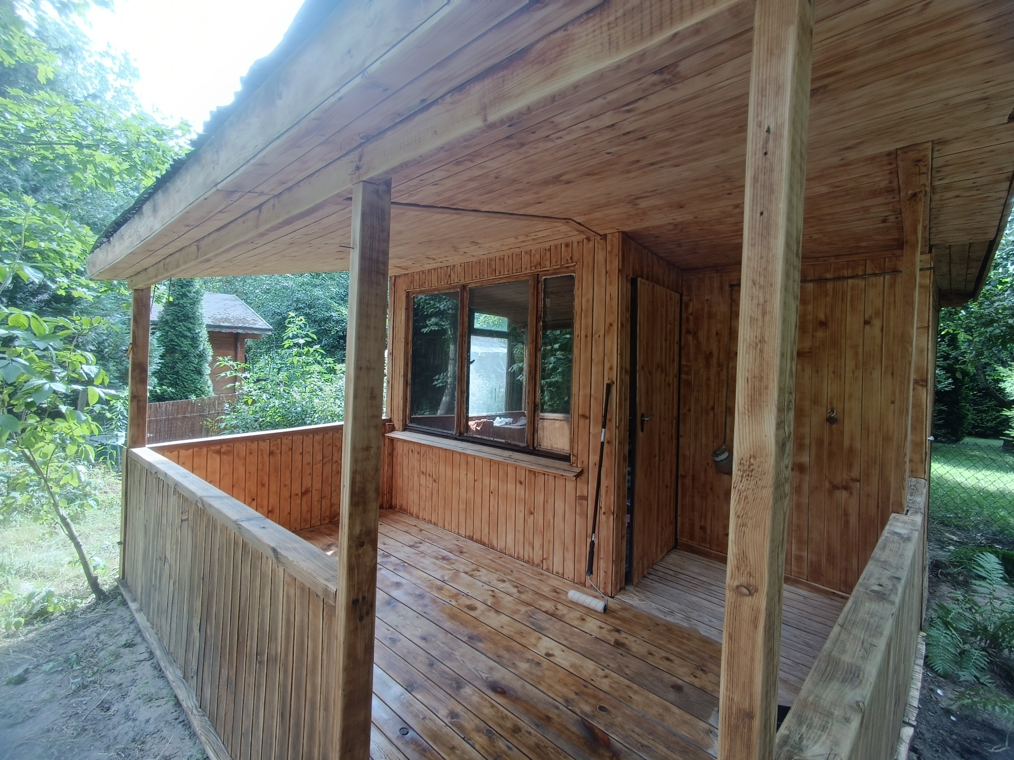 Drewniana altana z balustradą i oknami, widok z zewnątrz, widoczne ślady impregnacji drewna i wałek do malowania na podłodze.