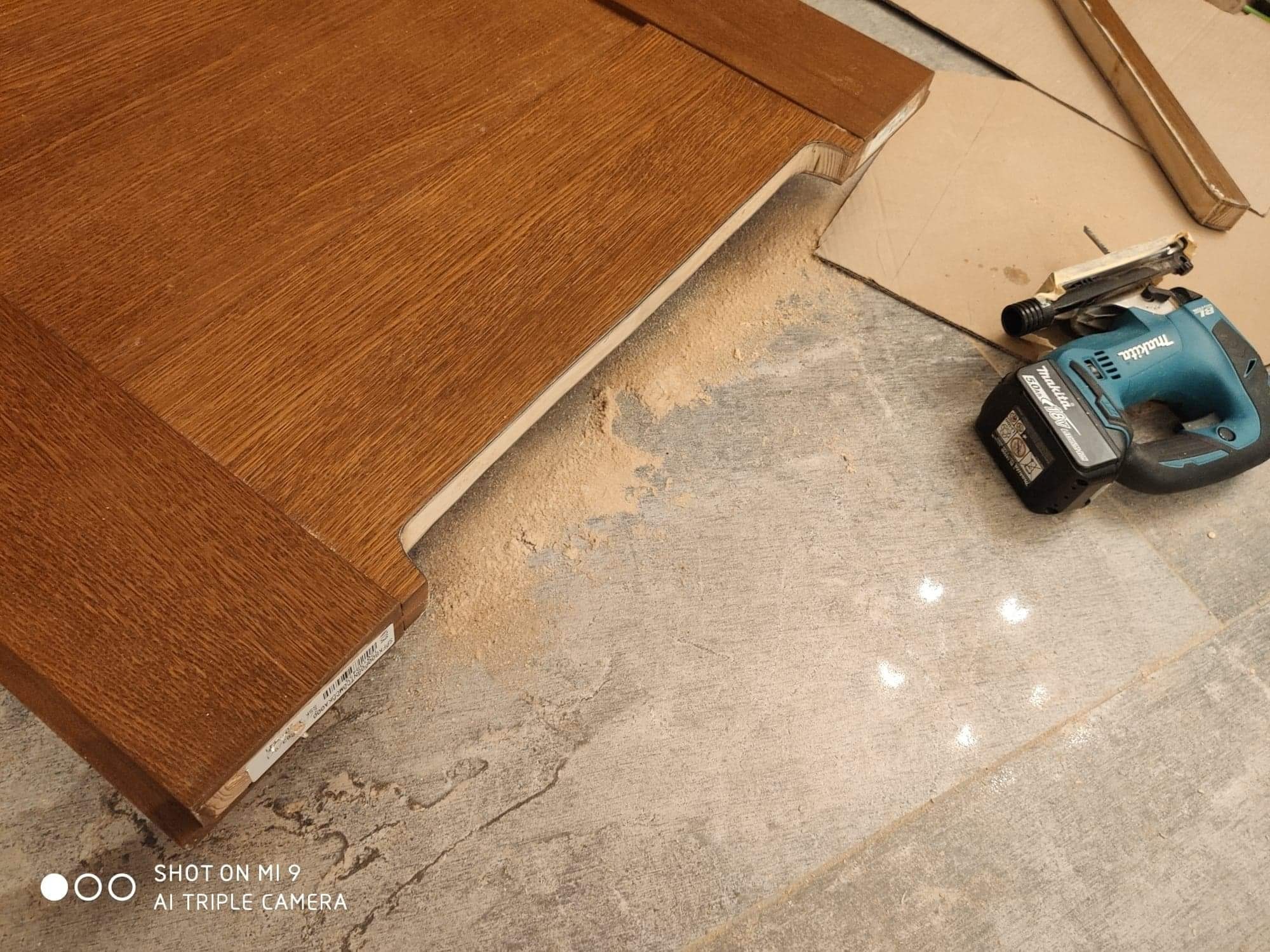 Fragment brązowego skrzydła drzwiowego z widocznymi śladami cięcia, obok leży wyrzynarka akumulatorowa Makita.