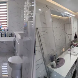 Nowoczesna łazienka z marmurowymi płytkami, kabiną prysznicową ze szklanym panelem, umywalką nablatową, pralką ukrytą pod blatem i dekoracyjnymi dodatkami.