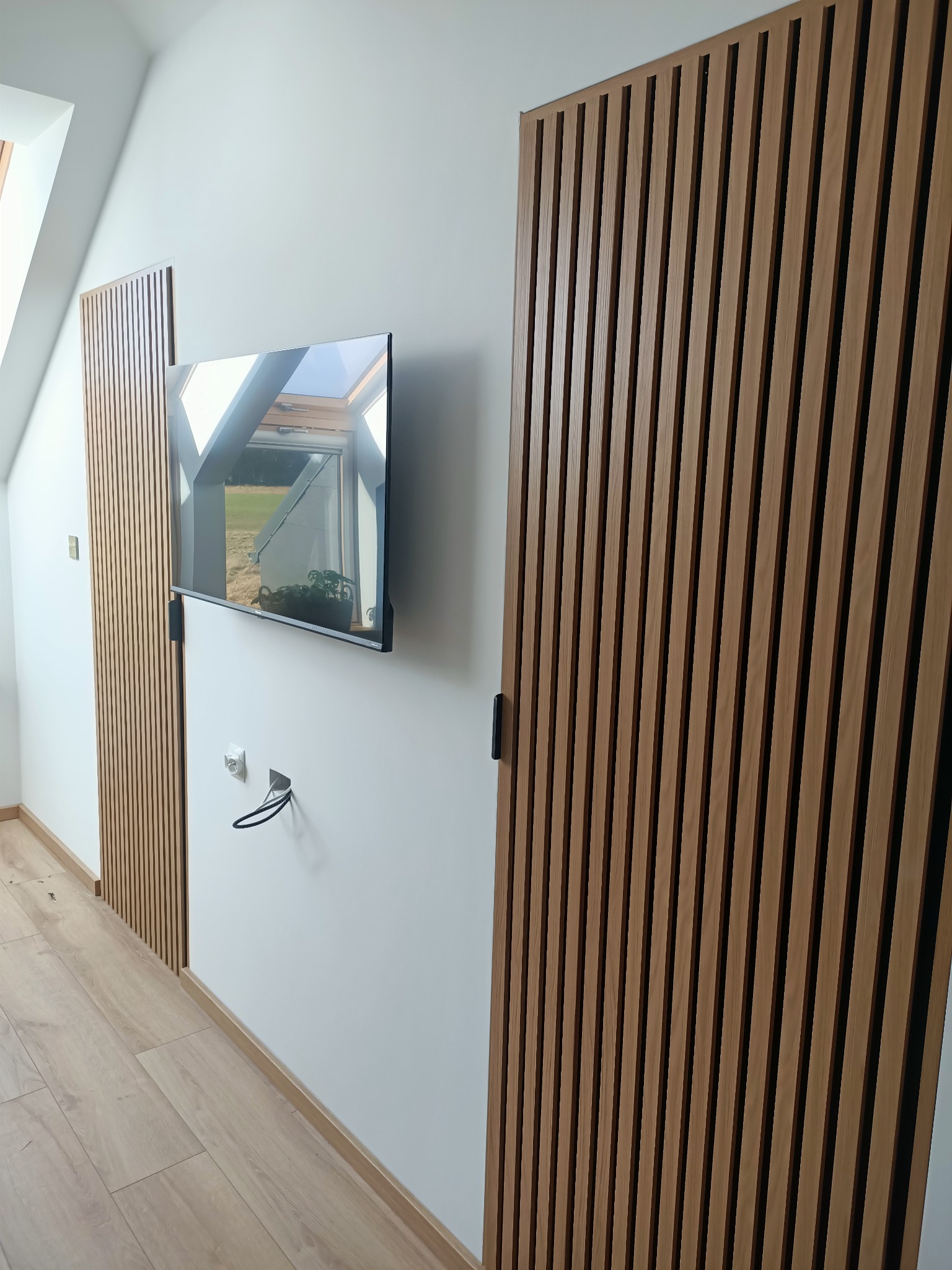 Drewniane panele ścienne w aranżacji wnętrza w Stargardzie, z telewizorem zamontowanym na ścianie i widokiem na okno dachowe.