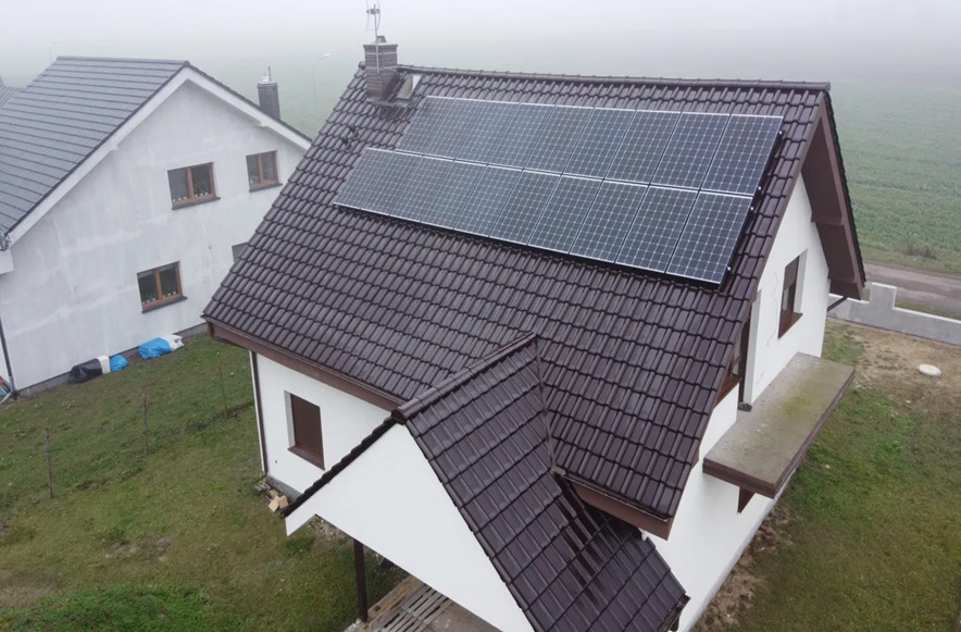Dwa panele fotowoltaiczne na brązowym dachu białego domu jednorodzinnego w mglisty dzień, widok z góry.