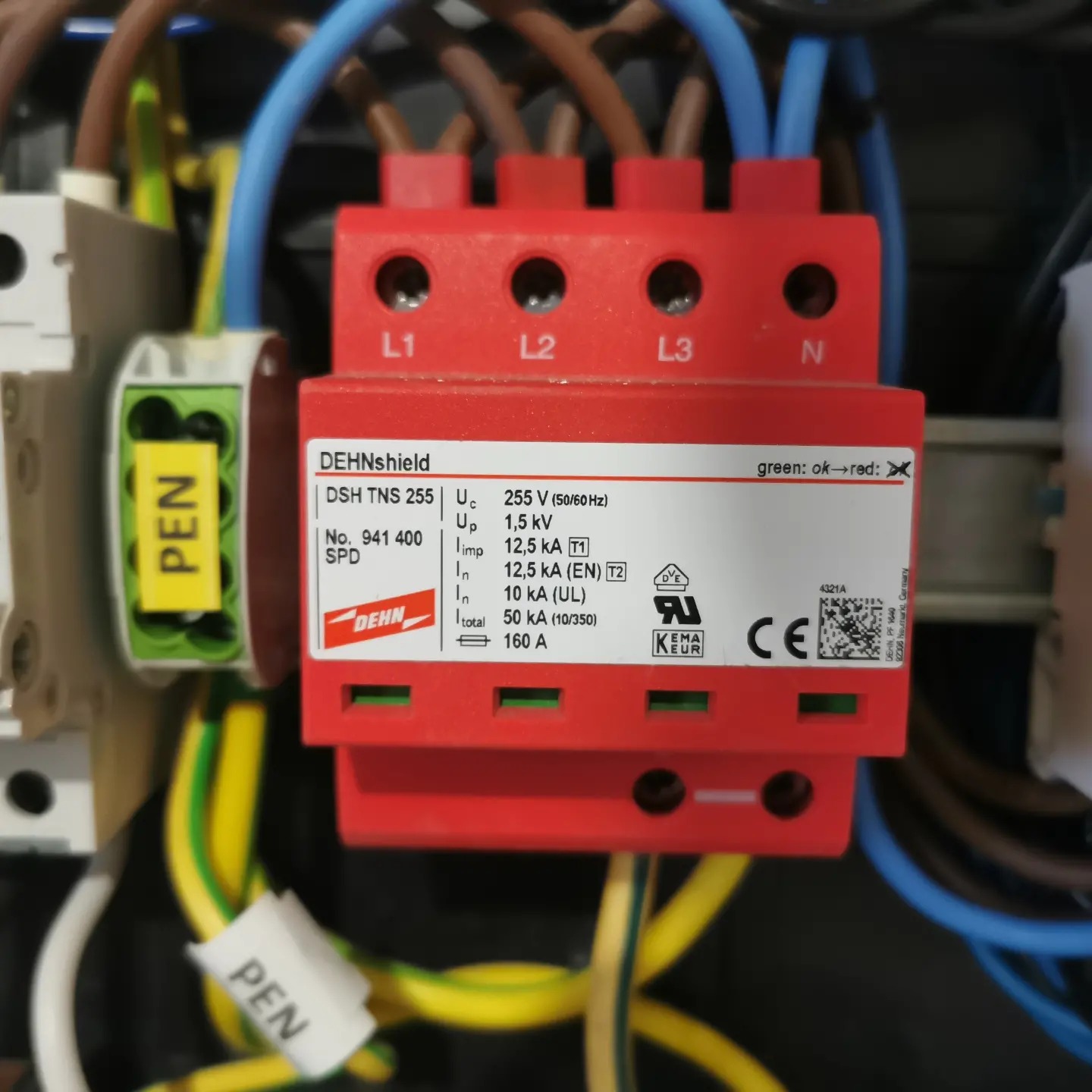 Czerwony ogranicznik przepięć DEHNshield DSH TNS 255 w rozdzielnicy elektrycznej, widoczne przewody z oznaczeniami PEN, etykieta z kodem QR i specyfikacją techniczną urządzenia.