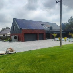 SamRemo - Nowoczesny dom jednorodzinny w Strzałkowie z panelami słonecznymi na dachu, wykończony czerwoną cegłą i szarym metalem, z dwustanowiskowym garażem i zadbanym trawnikiem.