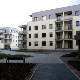 Usługi Inżynierskie RTK-BUD Robert Kmiecik - Nowoczesny kompleks apartamentów z balkonami, widok z poziomu dziedzińca z brukowaną ścieżką i elementami zieleni. Minimalistyczna architektura.